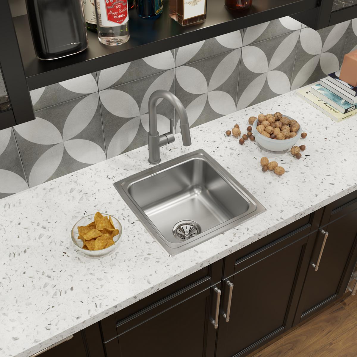 Stainless steel single bowl drop-in sink installed in white countertop with arched faucet and drain basket visible.