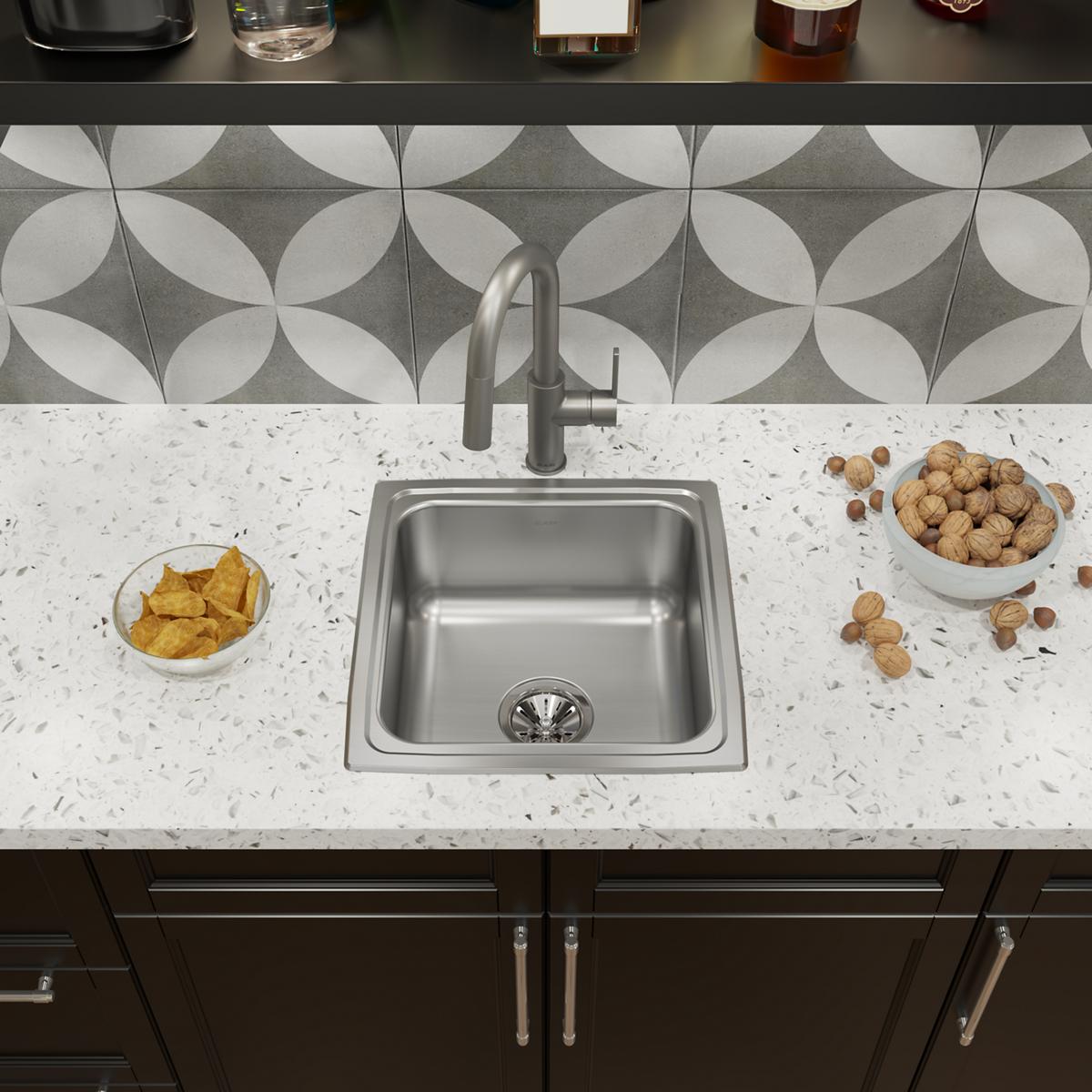 Stainless steel drop-in sink with single bowl installed in white countertop with faucet and drain visible.