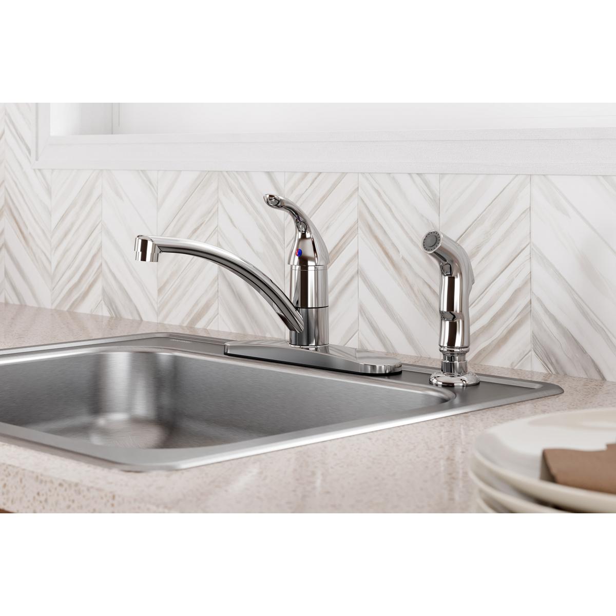 Chrome kitchen faucet with single lever handle and side spray mounted on sink deck with stainless steel sink.