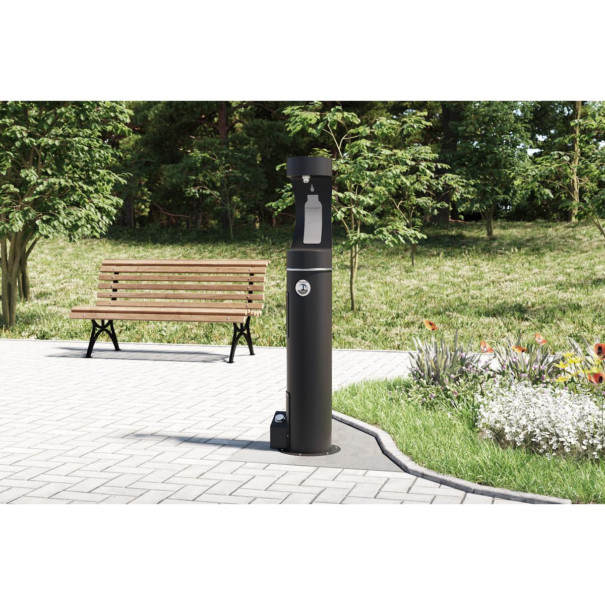 Black outdoor bottle filler pedal accessory mounted on ground-level post with foot pedal at base.