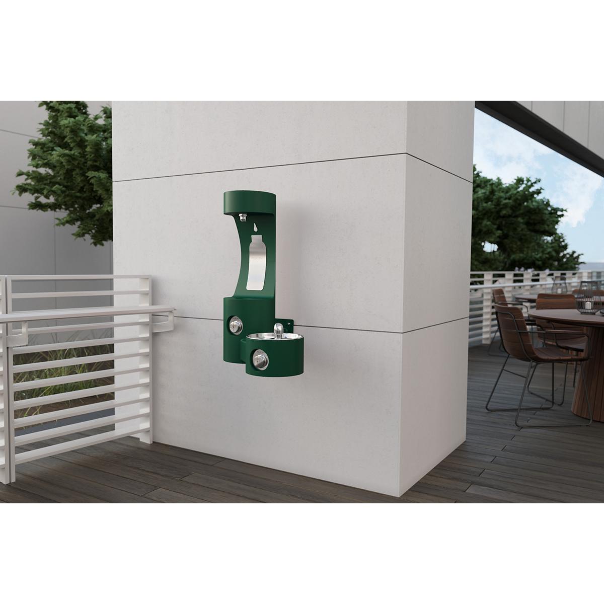 Evergreen wall-mounted bottle filling station with single drinking fountain spout and basin mounted on white exterior wall.