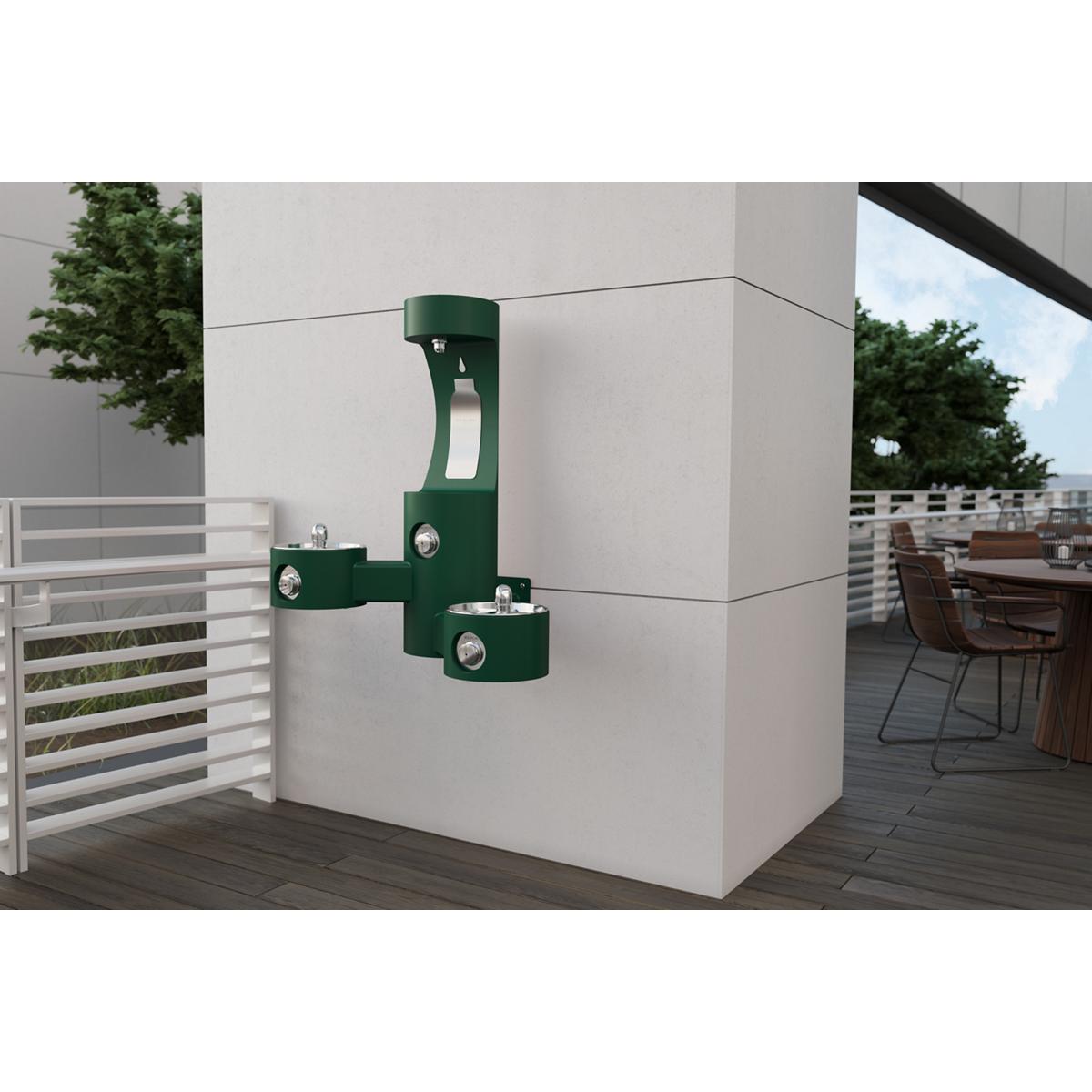 Green wall-mounted outdoor water fountain with two fill spouts attached to white building exterior.