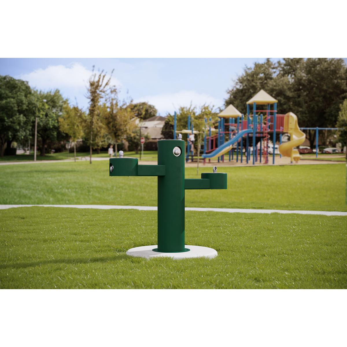 Green pedestal fountain with three staggered water bowls installed in outdoor park setting.