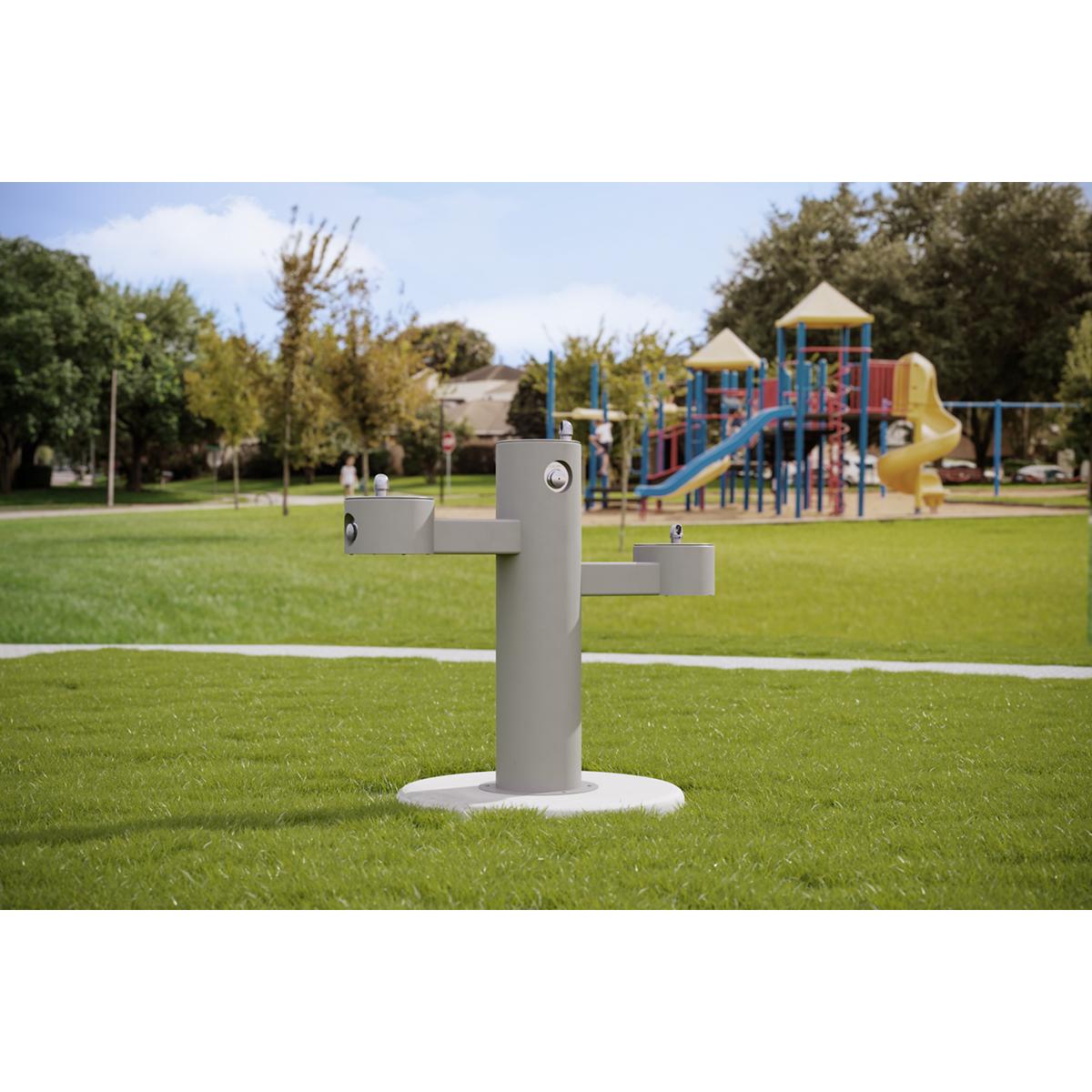 Gray pedestal fountain with three tiered drinking levels installed in an outdoor park setting on grass.