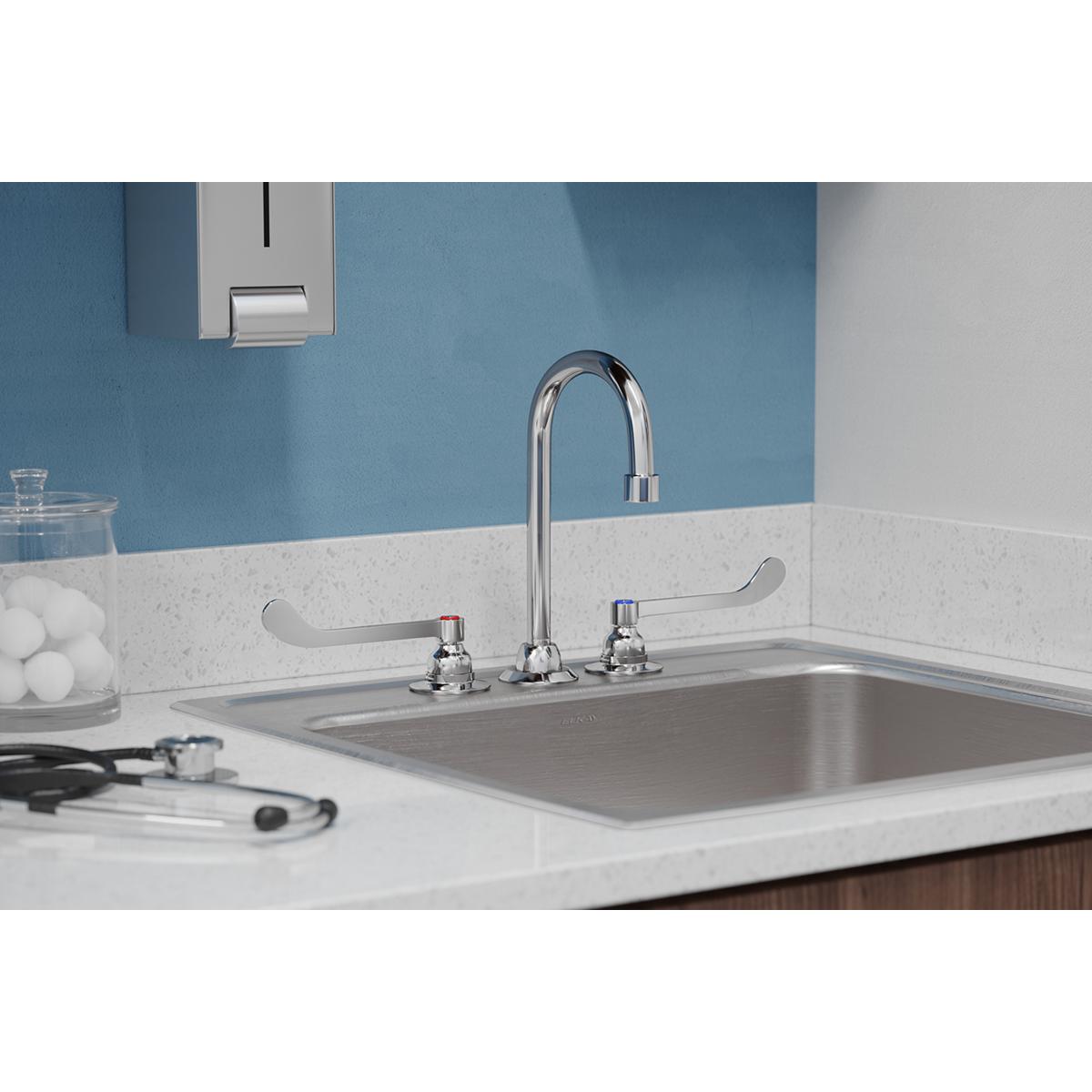 Chrome faucet with curved gooseneck spout and wristblade handles installed on kitchen sink countertop.