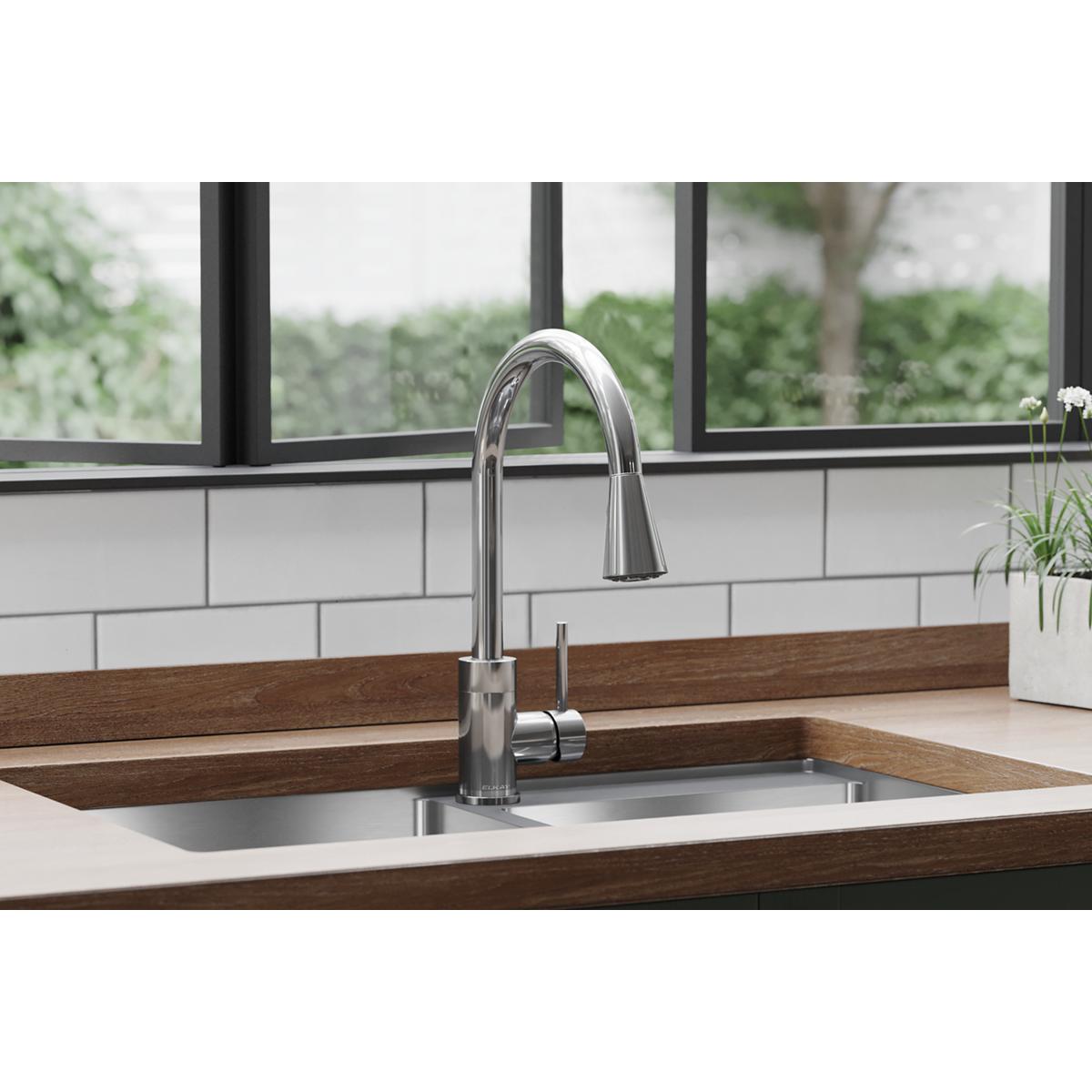 Chrome kitchen faucet with curved spout, pull-down spray, and forward lever handle installed in sink.