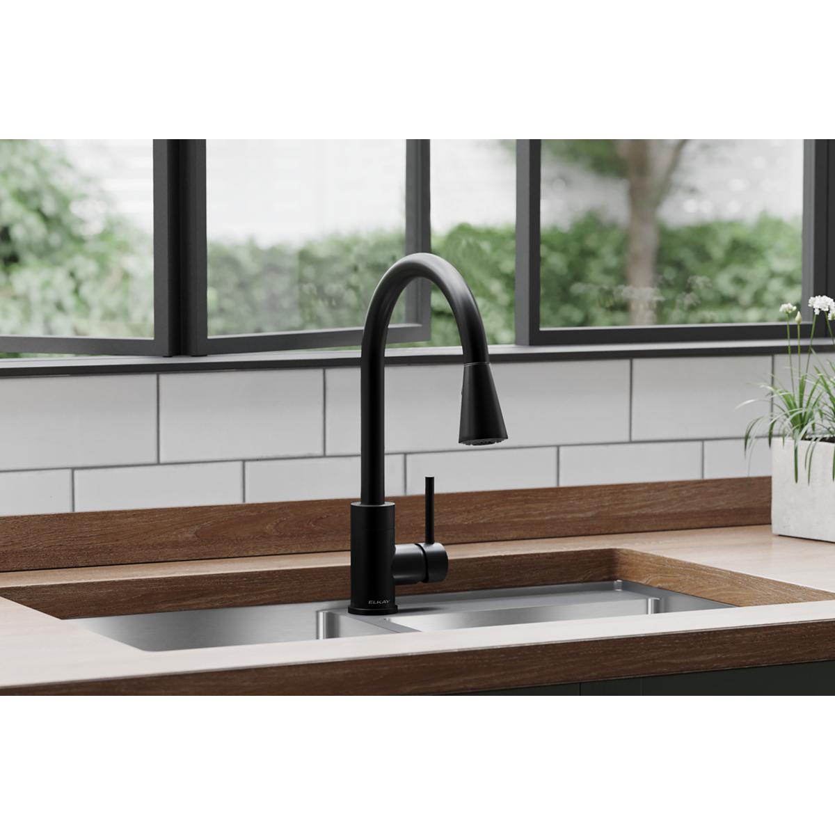 Matte black single-hole kitchen faucet with curved spout and pull-down spray mounted on white sink in wooden countertop.