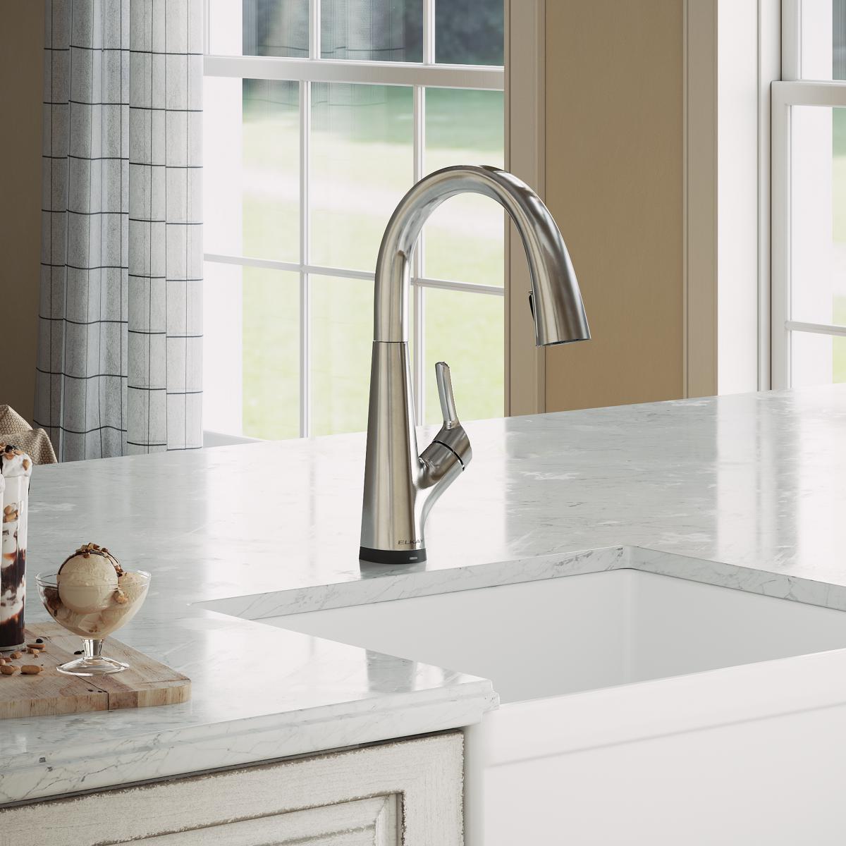 Chrome kitchen faucet with curved spout and side lever handle mounted on white marble countertop above white sink.