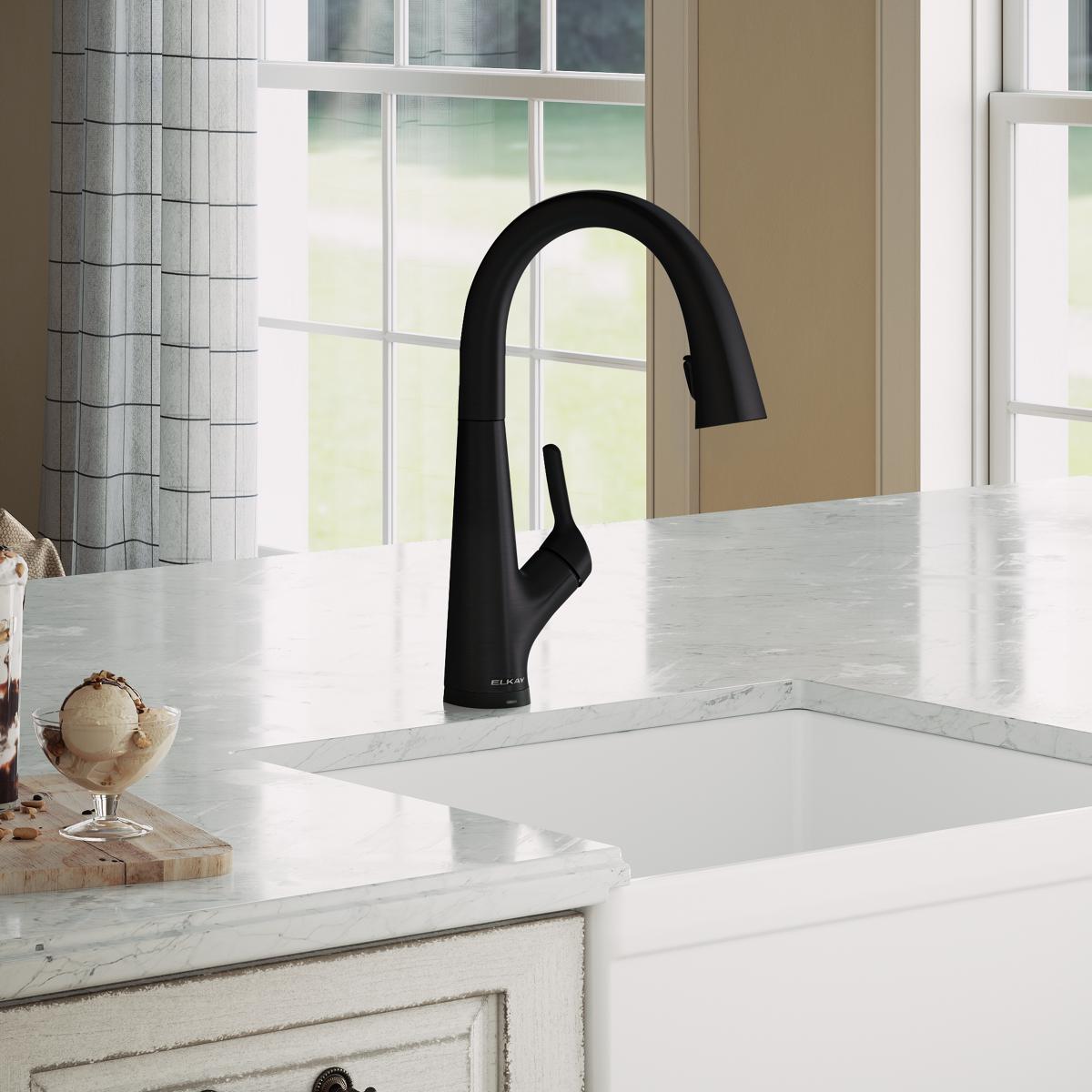 Matte black single-hole kitchen faucet with curved pull-down spout mounted on white marble countertop above sink.
