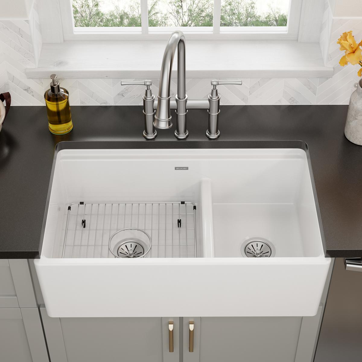 Stainless steel sink grid with vertical slat design and black mounting clips for double-bowl farmhouse sink.