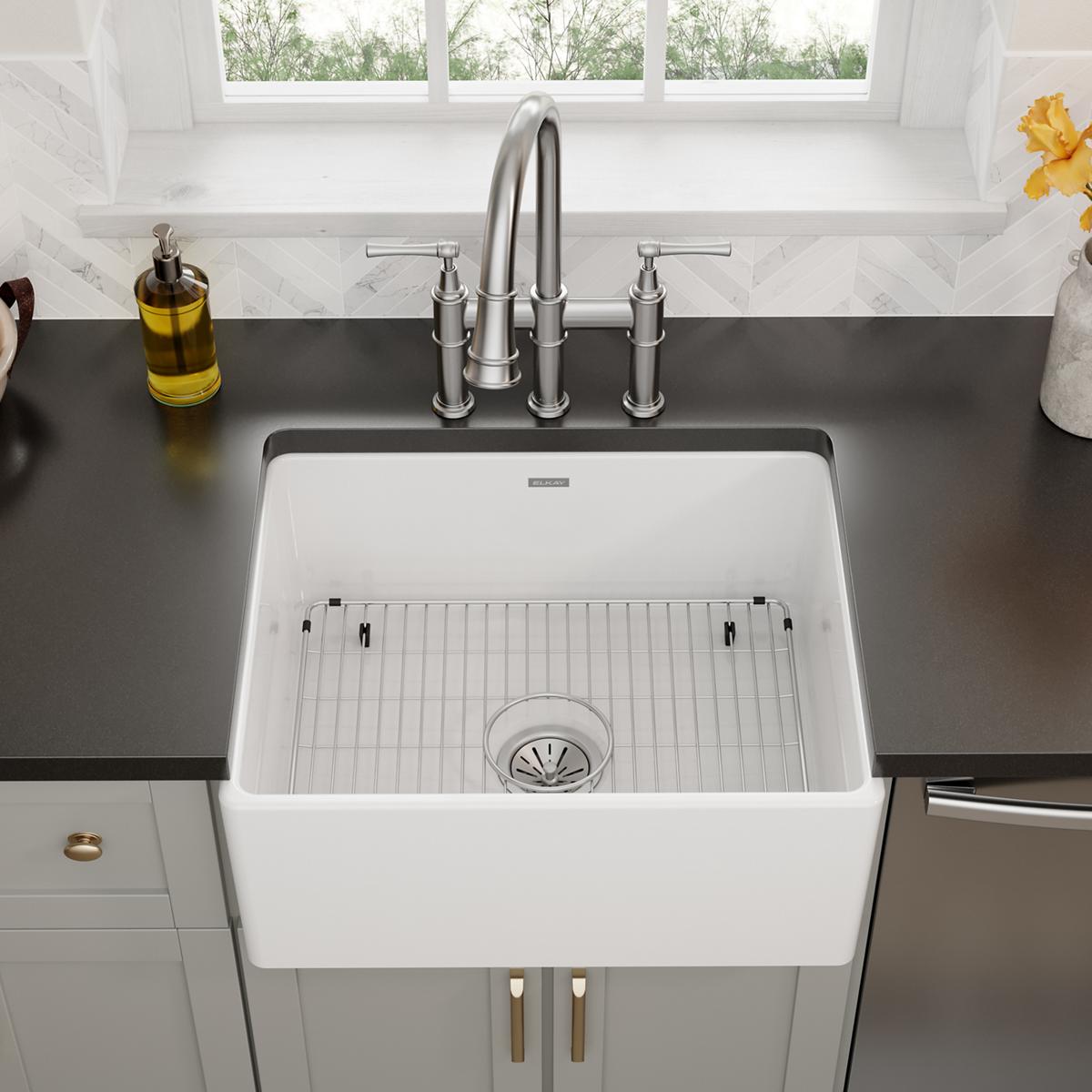 Stainless steel grid with vertical ribs and black mounting clips designed to fit inside a white farmhouse sink basin.