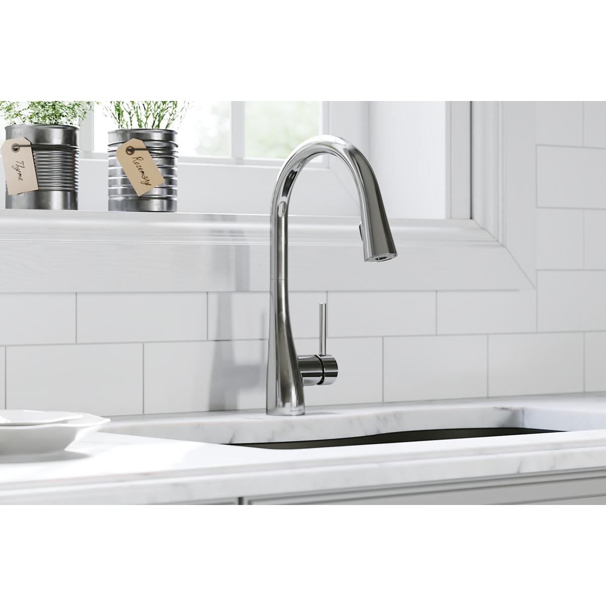 Chrome kitchen faucet with curved spout and pull-down spray mounted on white countertop with subway tile backsplash.