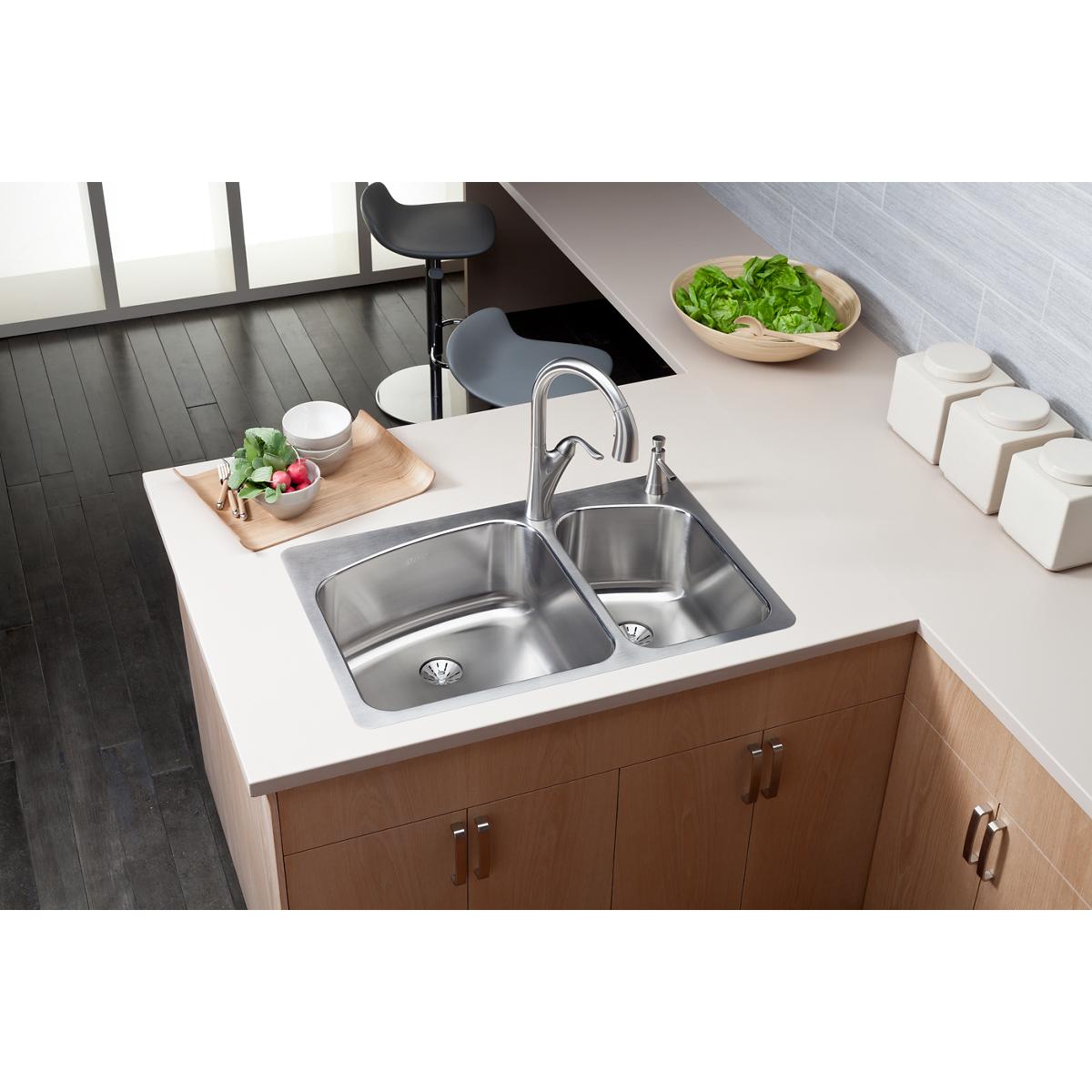 Stainless steel double bowl sink with larger left basin and smaller right basin, mounted in white countertop with chrome fauc