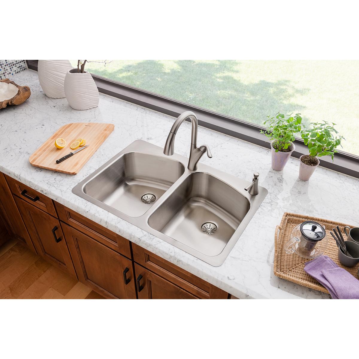 Stainless steel double bowl sink with two drain holes mounted in white countertop, paired with curved faucet.