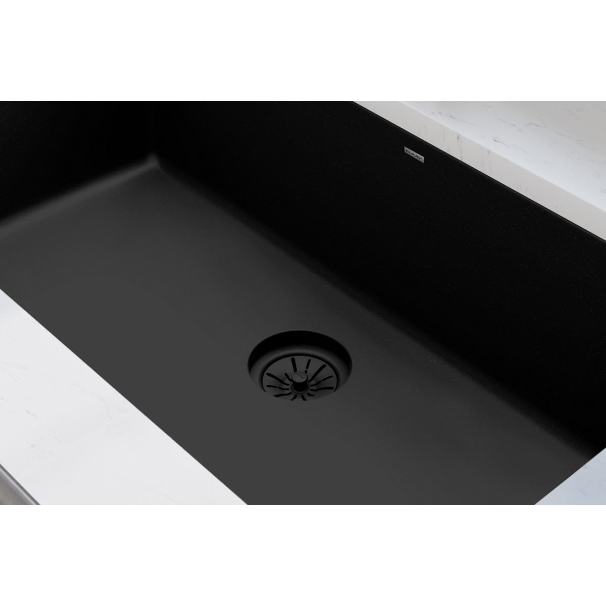 Black polymer sink drain flange with radial strainer basket pattern in dark quartz sink basin.