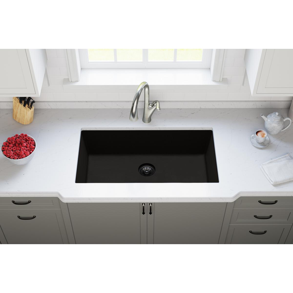 Black polymer sink with round drain opening installed in white countertop with faucet.