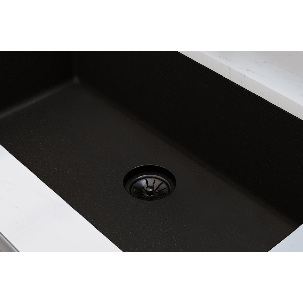 Black polymer sink drain flange with basket strainer installed in dark composite sink bowl.