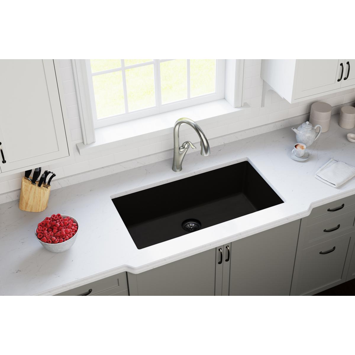 Black quartz undermount sink with drain flange installed in white kitchen countertop.
