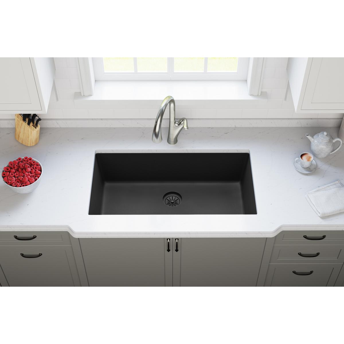 Charcoal polymer sink basin with drain opening and faucet installed in white kitchen countertop.