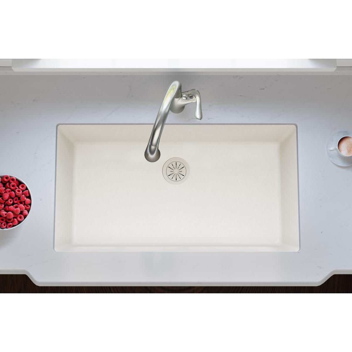 Parchment polymer sink drain flange with circular strainer basket insert and rubber stopper visible in white composite sink.