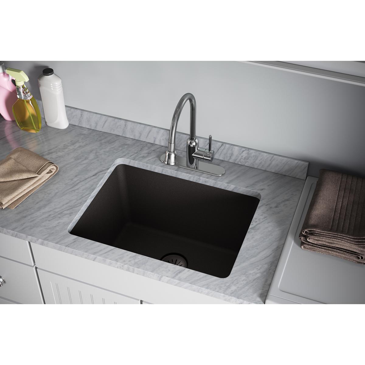 Black quartz composite sink with chrome faucet installed in marble countertop.
