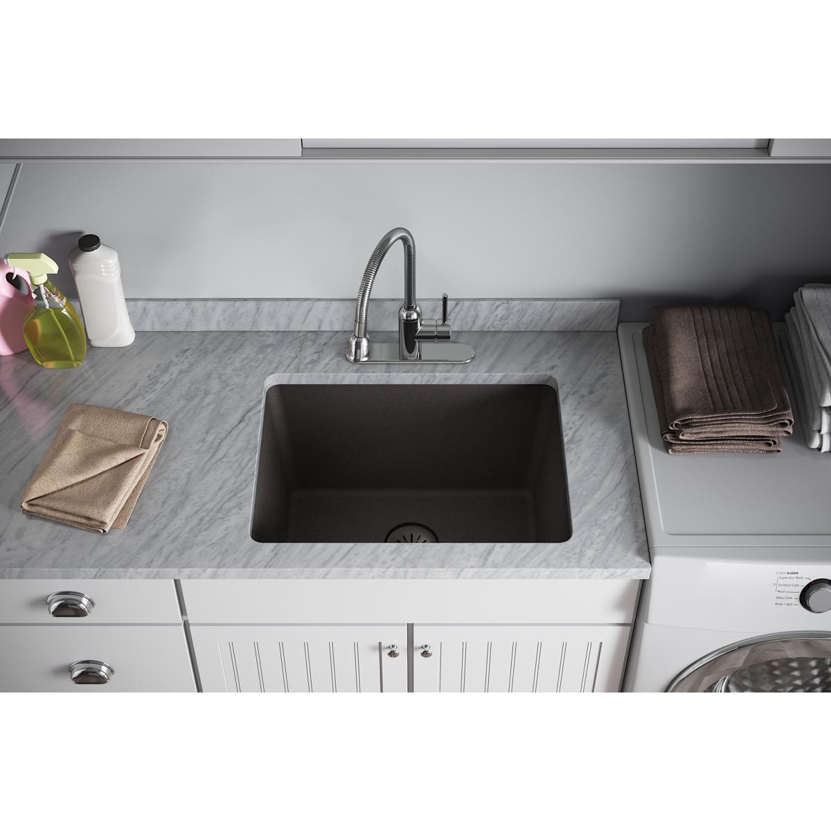 Black quartz sink with chrome faucet installed in marble countertop kitchen.