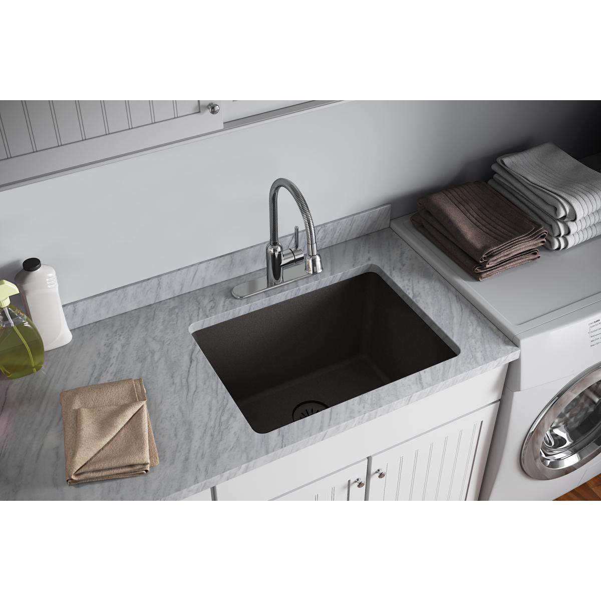 Black quartz sink basin with chrome faucet installed in white cabinetry with marble countertop.