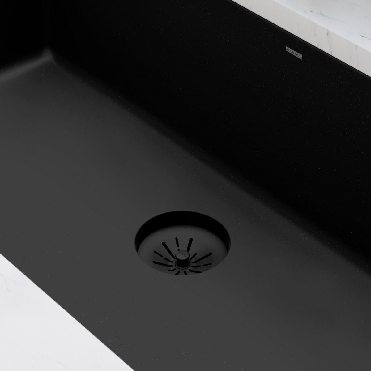Black polymer basket strainer with radiating slots installed in dark quartz sink drain opening.