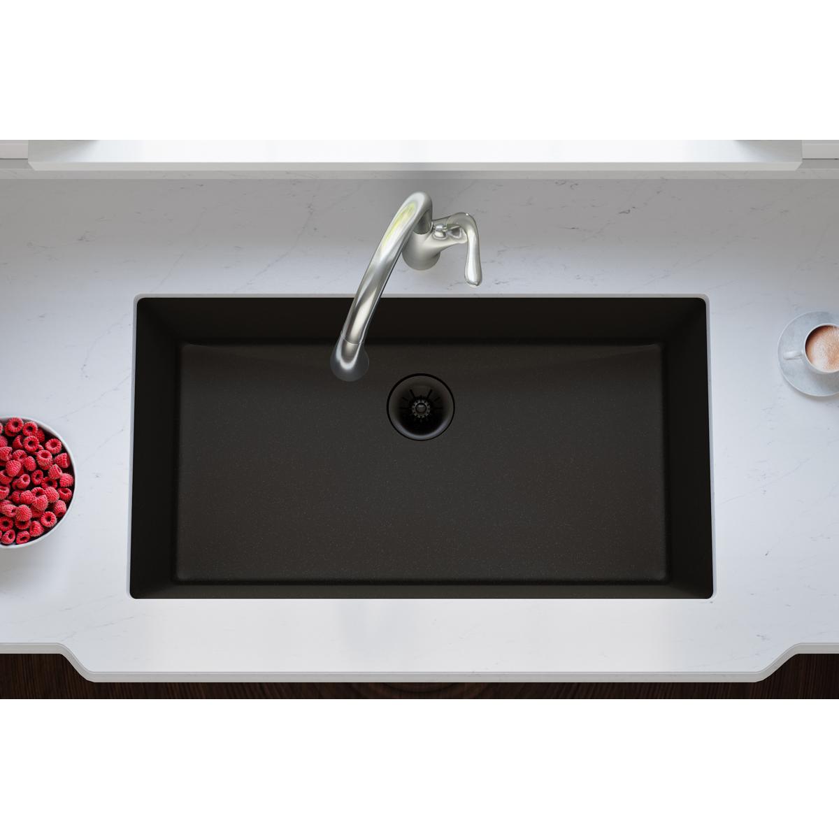 Black quartz sink bowl with chrome faucet and circular drain strainer viewed from above.