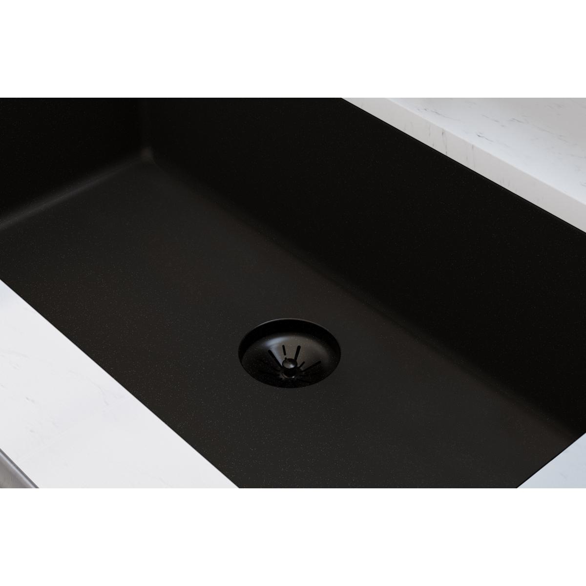 Black polymer basket strainer with rubber stopper installed in dark quartz sink drain.