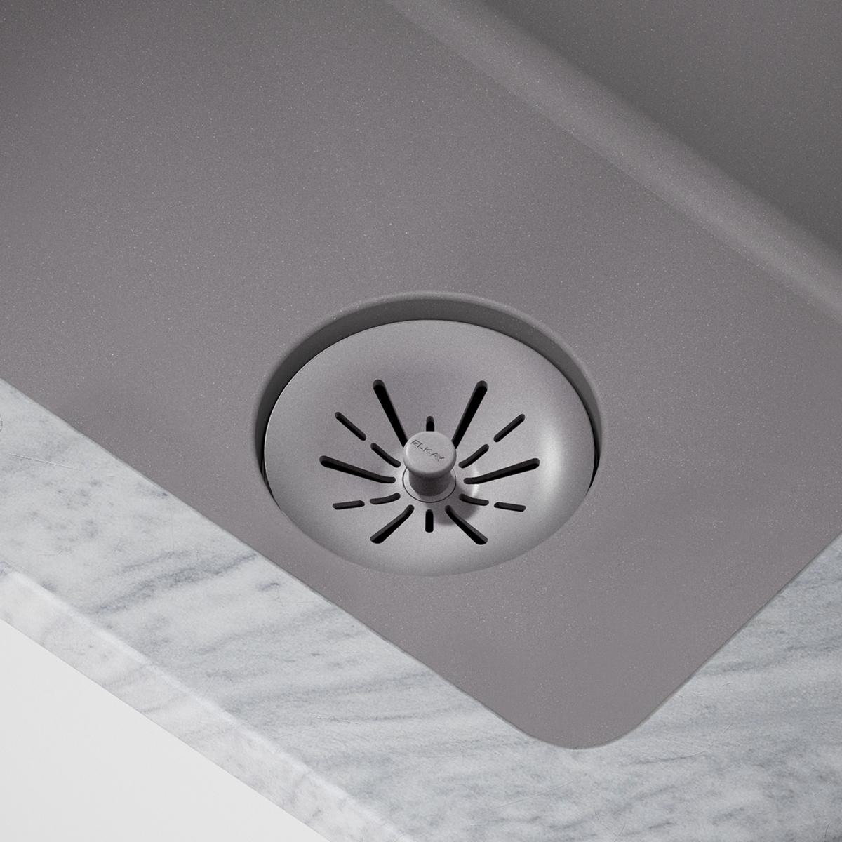 Greystone polymer basket strainer with radial slots and central knob installed in sink drain opening.