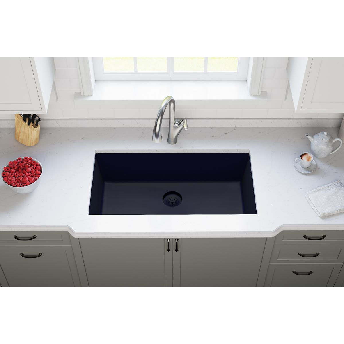 Black quartz undermount kitchen sink with drain opening visible in white countertop.
