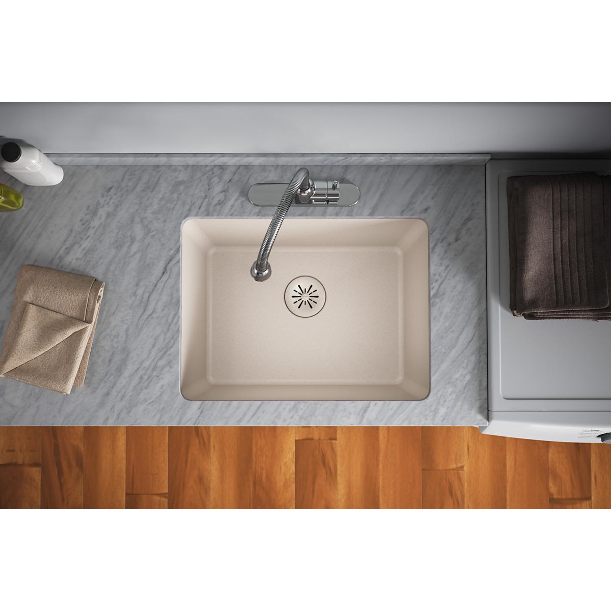 Overhead view of a beige quartz kitchen sink with a drain basket strainer and faucet installed on a marble countertop.