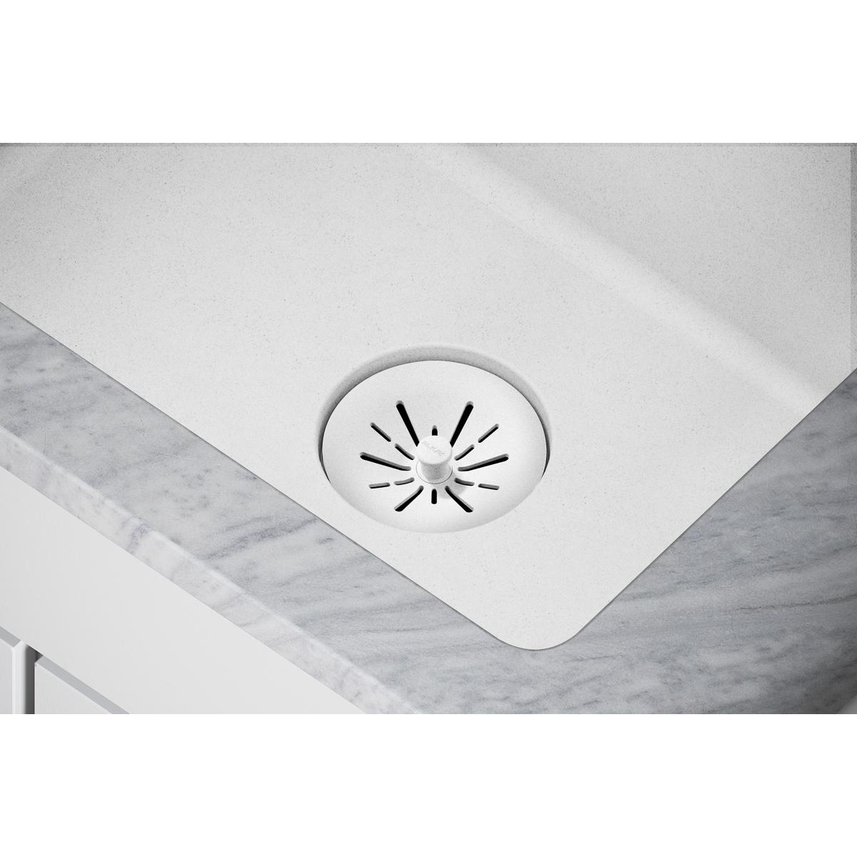 White polymer basket strainer with radial slot pattern installed in quartz sink drain opening.