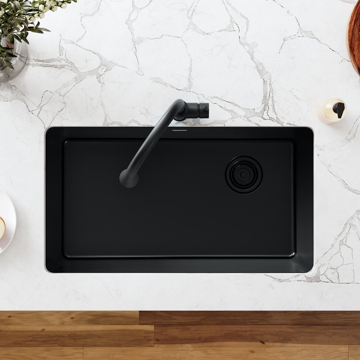 Black polymer sink with curved drain fitting and basket strainer outlet, overhead view.