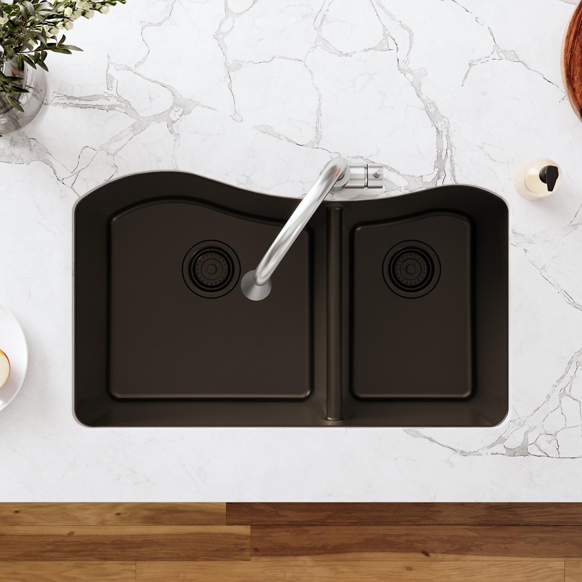 Black polymer double-bowl sink with silver faucet and visible drain fittings, viewed from above on marble countertop.