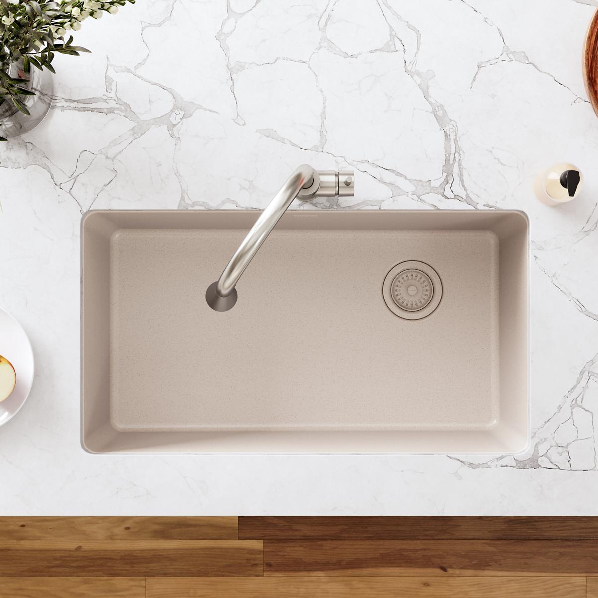 Taupe polymer sink basin with stainless steel drain fitting and removable basket strainer, viewed from above.