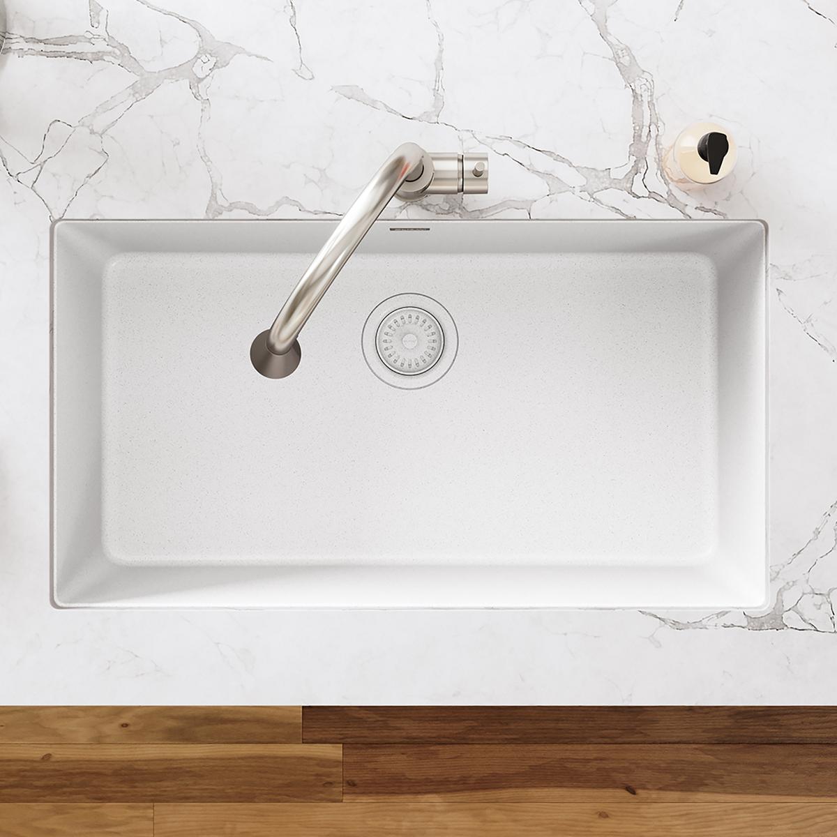 White polymer sink with stainless steel faucet and circular drain fitting with basket strainer visible in basin.