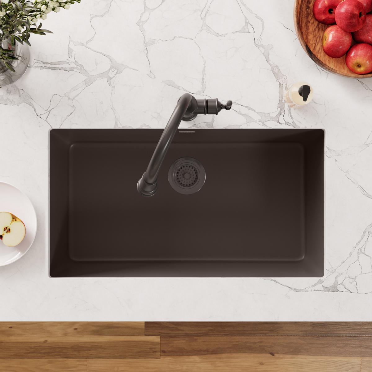 Antique steel drain fitting with basket and rubber stopper installed in black sink basin.
