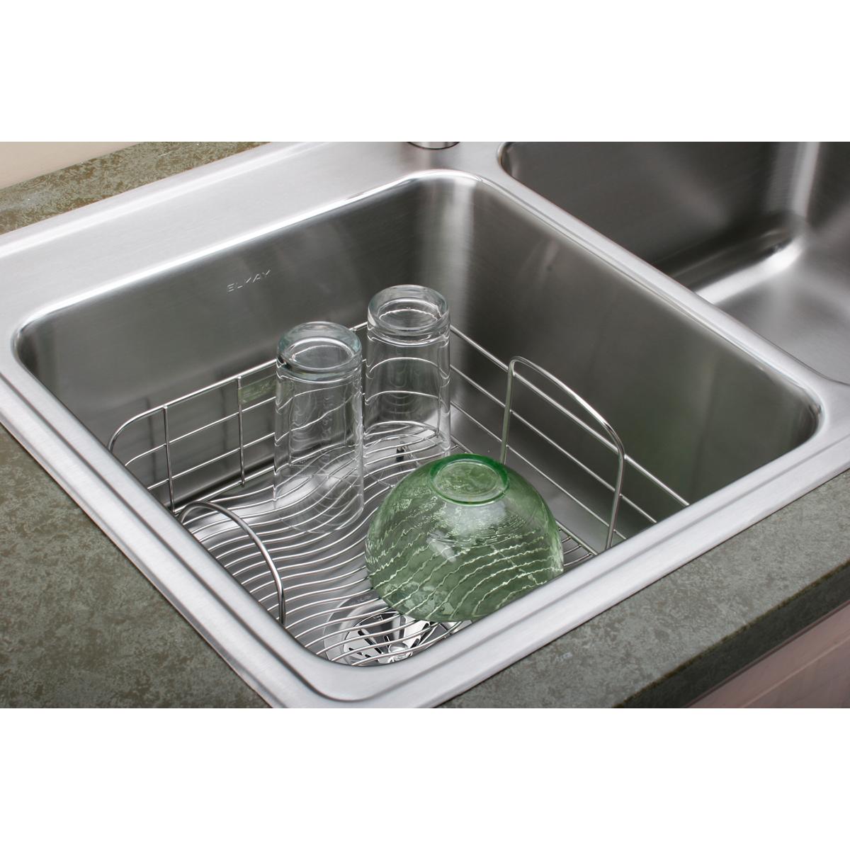Stainless steel rinsing basket with divided compartments holding glass jars and a green bowl, positioned in a kitchen sink.