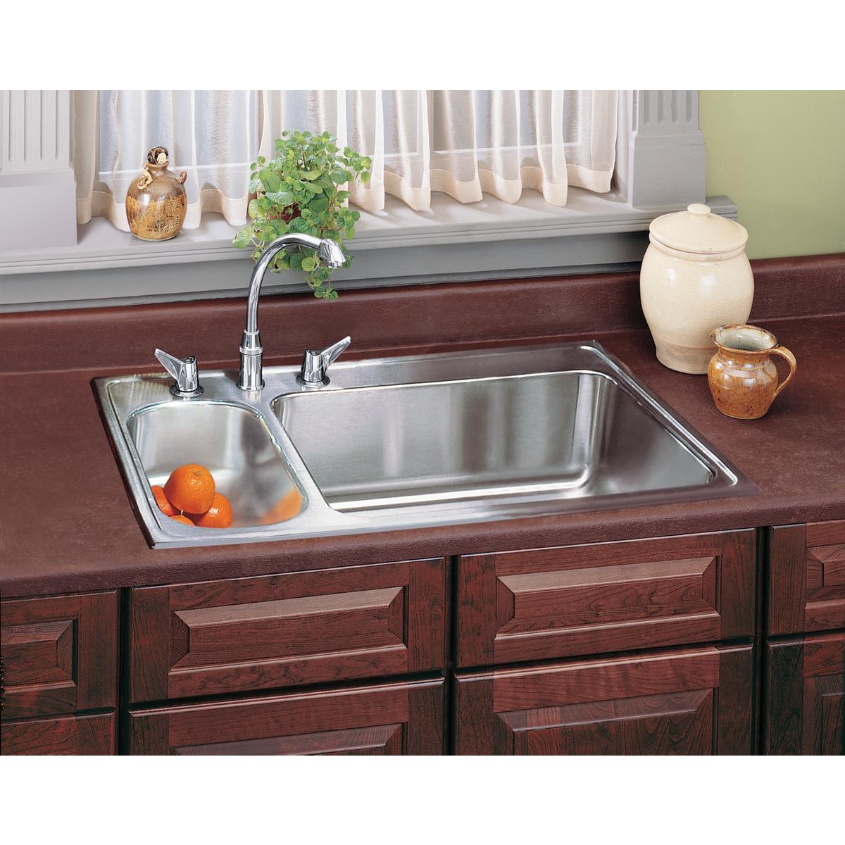 Stainless steel drop-in sink with two unequal bowls and chrome faucet installed in dark wood countertop.