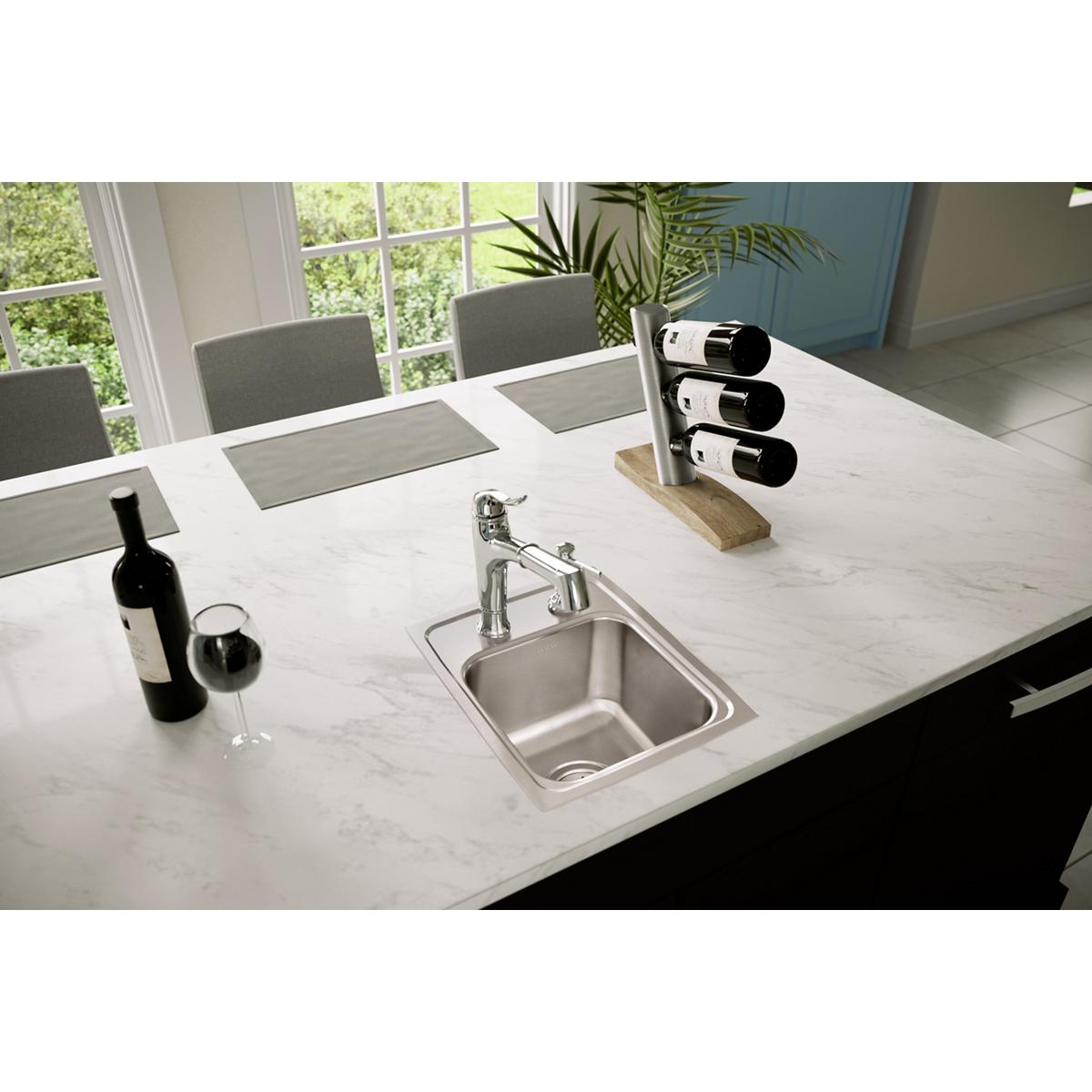 Stainless steel single bowl drop-in sink with two faucet holes installed in white countertop.
