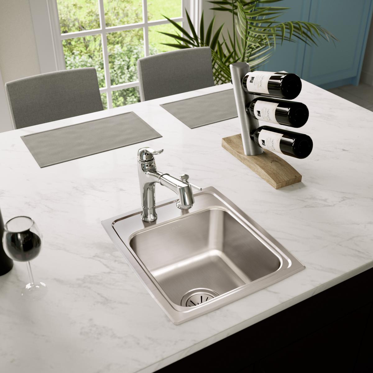 Stainless steel drop-in bar sink with single bowl and chrome faucet installed in white marble countertop.