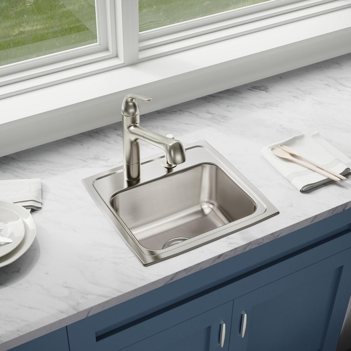 Stainless steel drop-in sink with single bowl and two faucet holes installed in marble countertop with matching faucet.