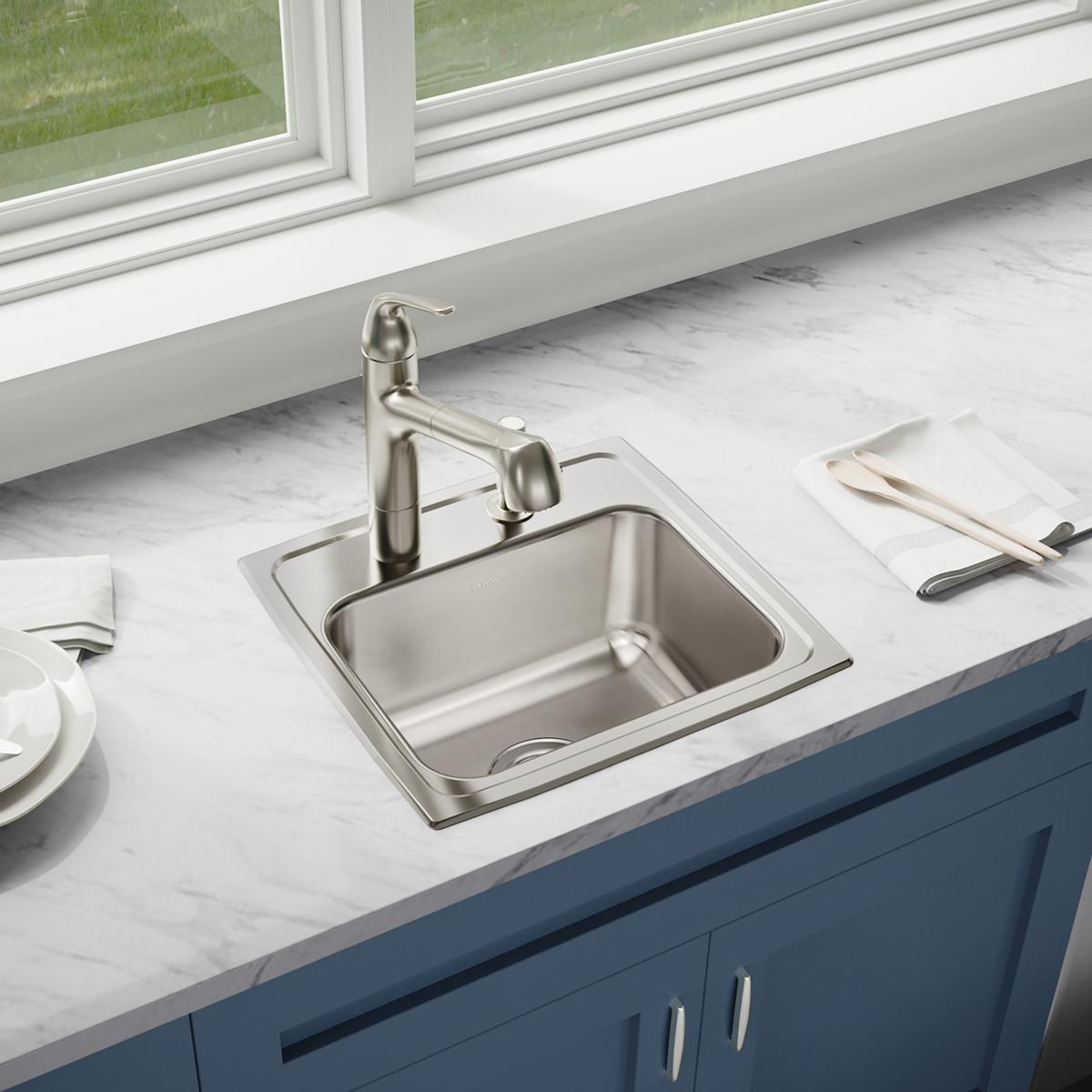 Stainless steel drop-in sink with single bowl and two-hole faucet mounted on marble countertop with blue cabinet base.