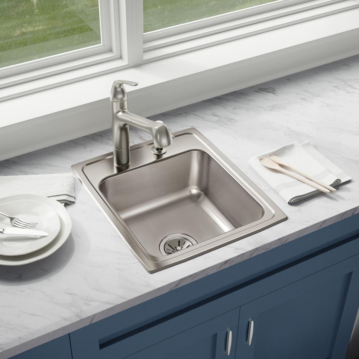 Stainless steel drop-in sink with single bowl and faucet installed in marble countertop with blue cabinetry below.