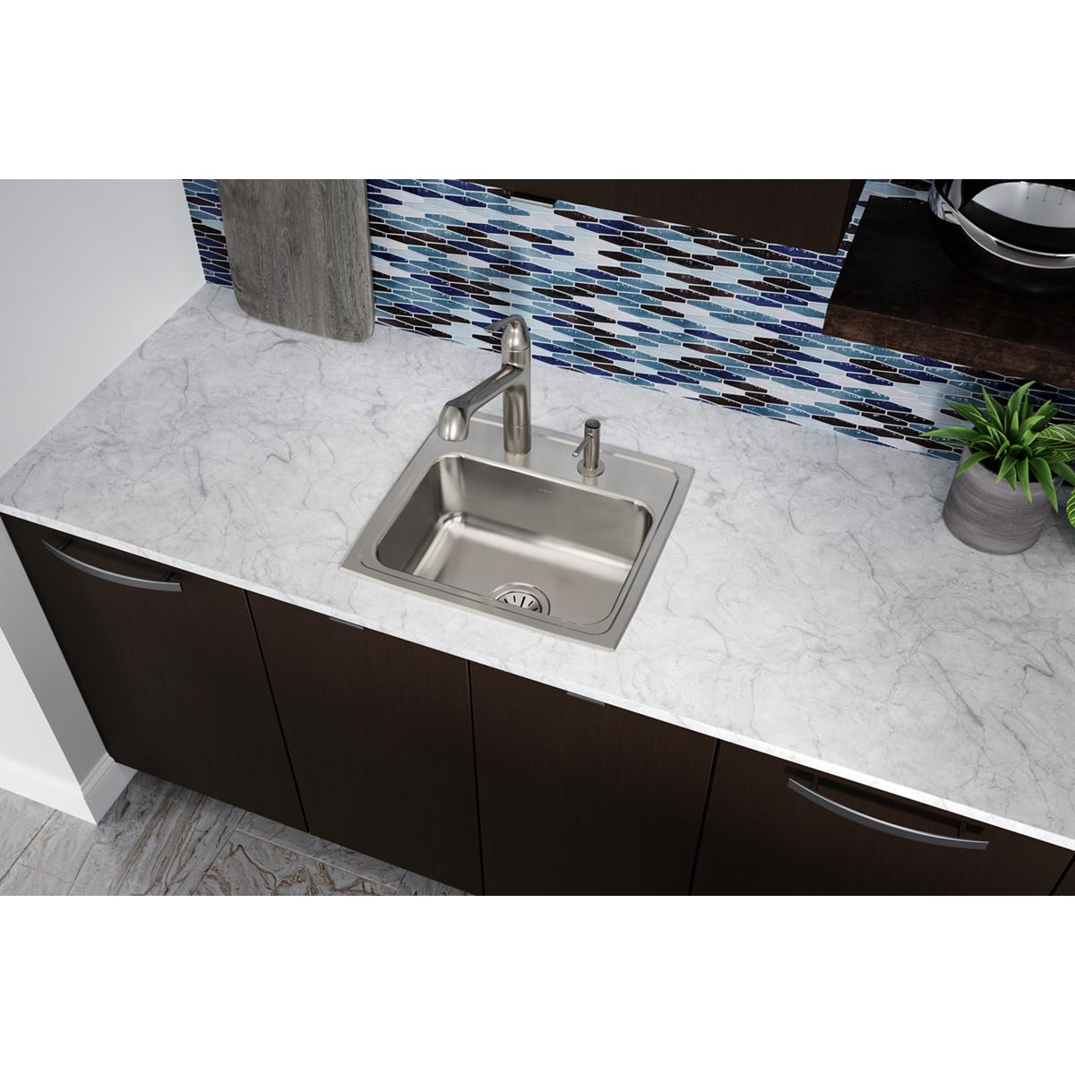 Stainless steel drop-in kitchen sink with single bowl and two pre-drilled faucet holes, installed in marble countertop.
