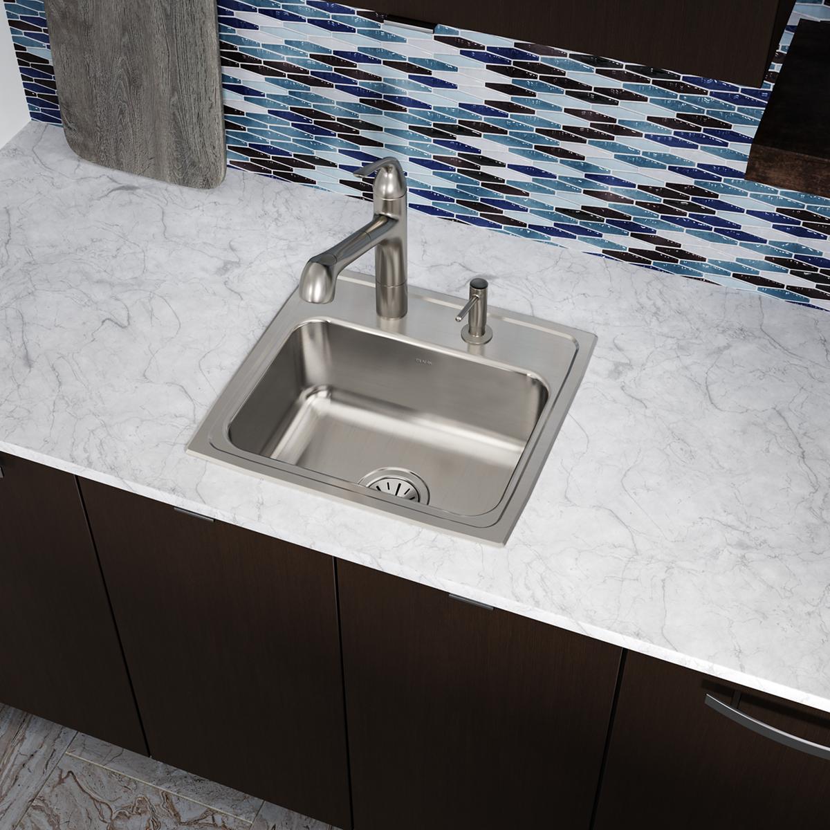 Stainless steel drop-in sink with single bowl, faucet, and soap dispenser mounted in marble countertop.