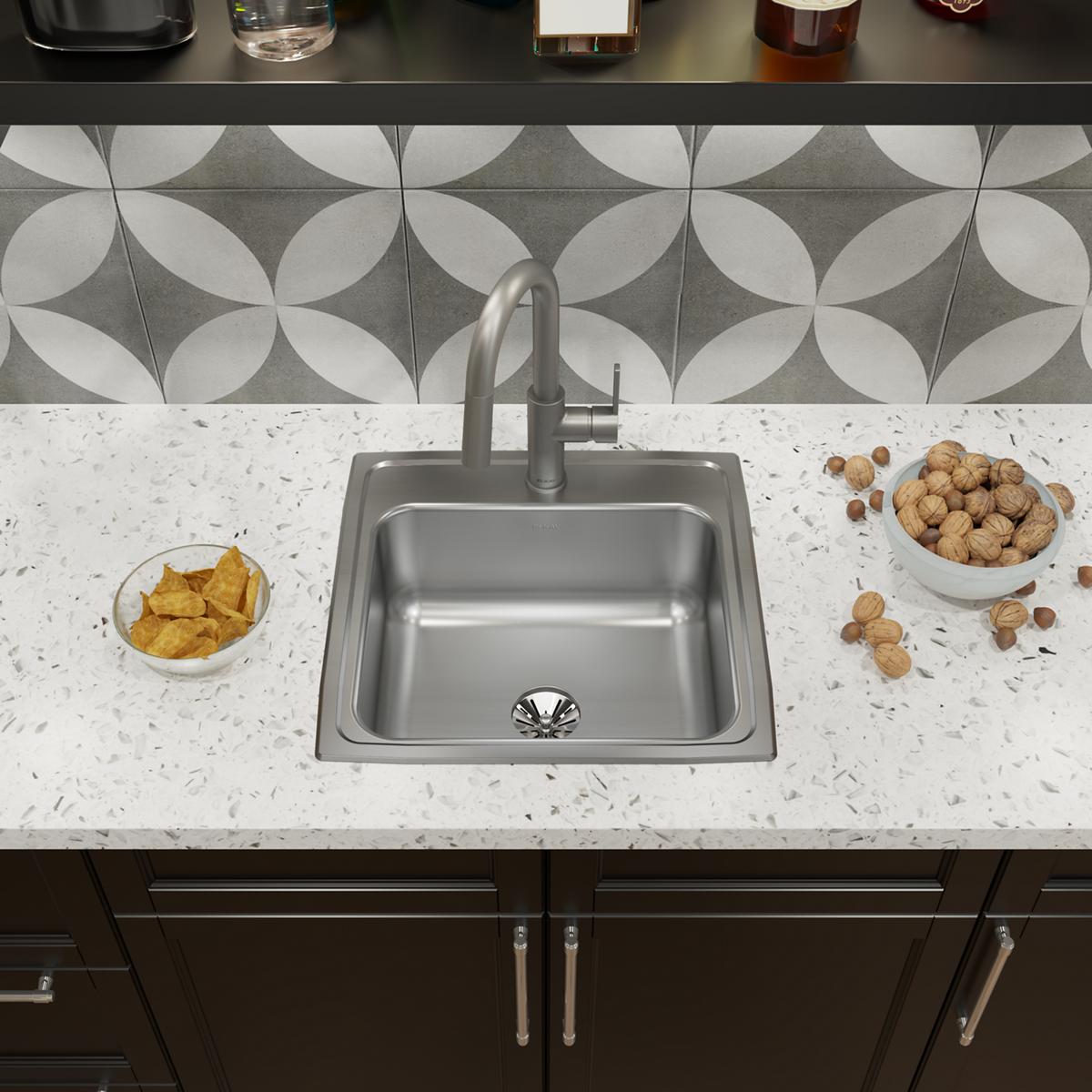 Stainless steel single bowl drop-in sink installed in white quartz countertop with faucet and drain visible.