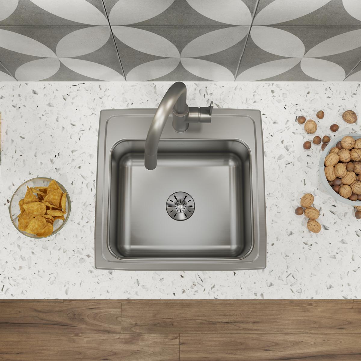 Stainless steel square drop-in sink with single bowl and drain strainer, mounted in white speckled countertop with chrome fau